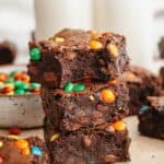A stack of M&M brownies, the brownie on top has a bite taken out of it.