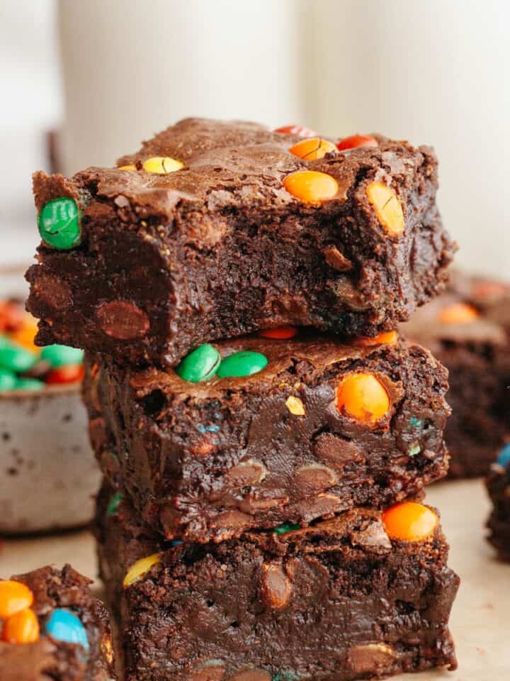 A stack of M&M brownies, the brownie on top has a bite taken out of it.