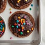 Cookies covered in chocolate ganache and rainbow chips on parchment paper.