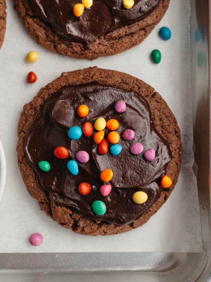 Cookies covered in chocolate ganache and rainbow chips on parchment paper.