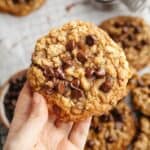 A hand holding a brown butter oatmeal cookie with chocolate chips.