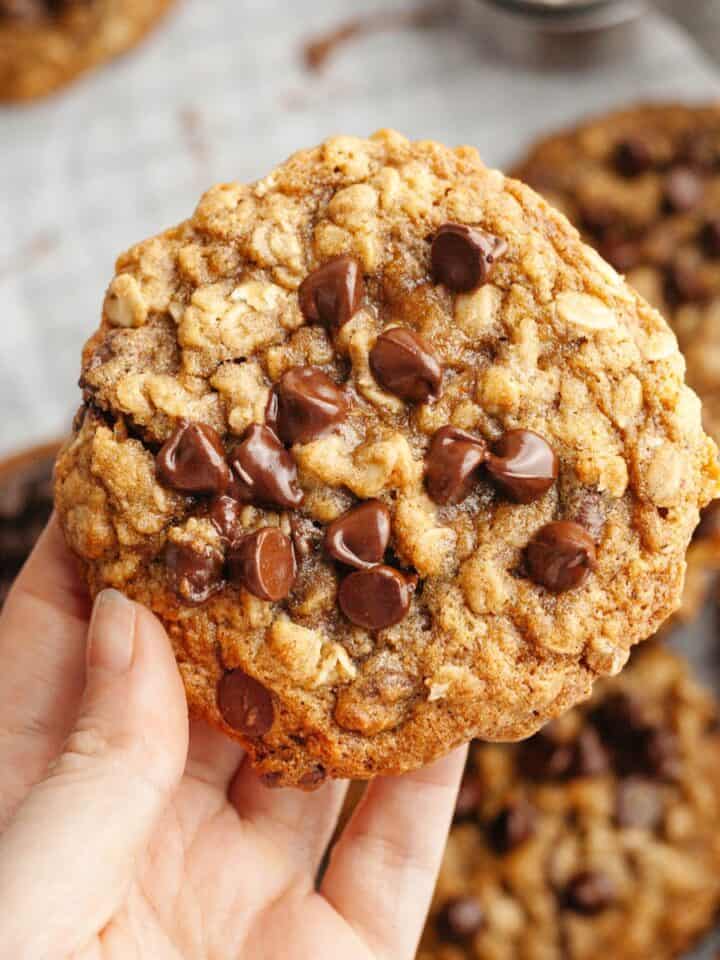 A hand holding a brown butter oatmeal cookie with chocolate chips.