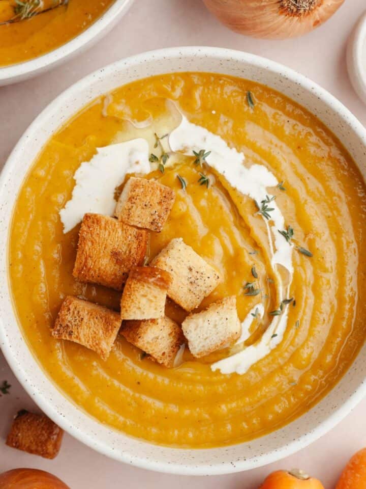 A white bowl with roasted carrot butternut squash soup and brioche croutons.
