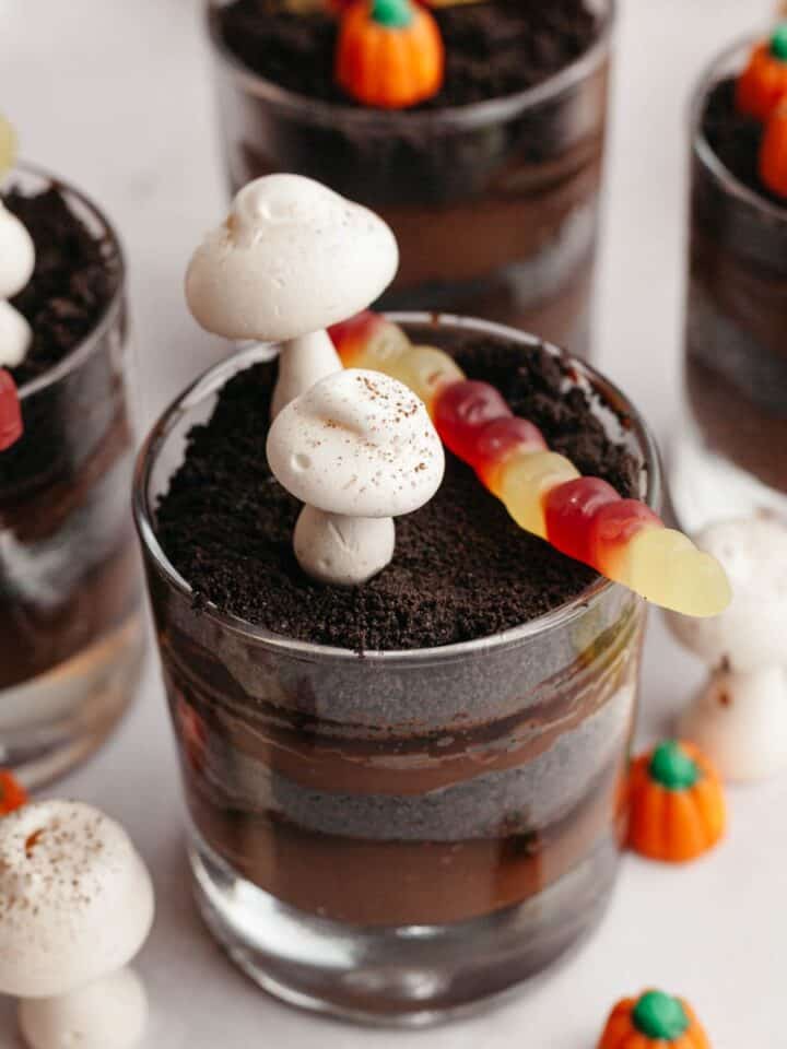 Glass cups with layers of chocolate pudding and Oreo cookie crumbs, decorated with meringue mushrooms and gummy worms.