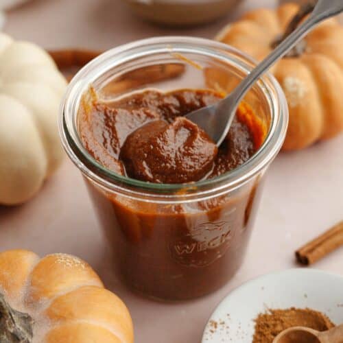 Pumpkin sauce in a glass jar with a spoon.