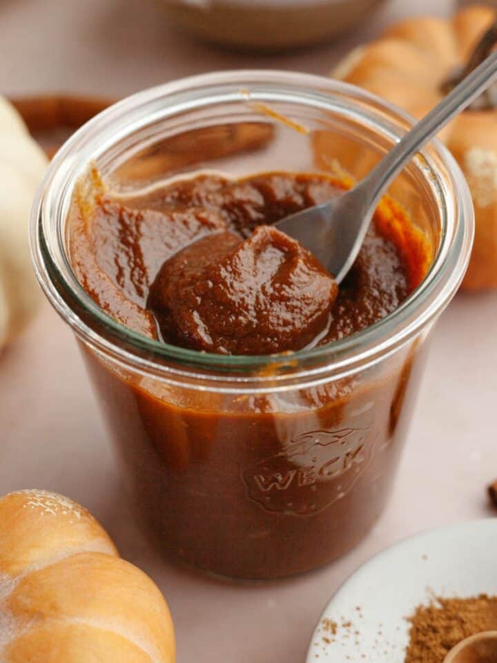 Pumpkin sauce in a glass jar with a spoon.