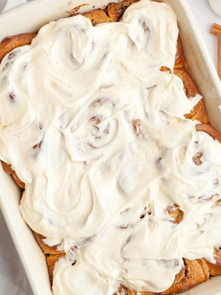 Brown butter cinnamon rolls covered with brown butter frosting in a white dish.