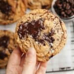 A hand holding a brown butter chocolate chip espresso cookies, sprinkled with some flaky sea salt.