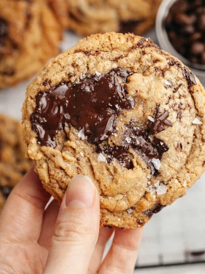 A hand holding a brown butter chocolate chip espresso cookies, sprinkled with some flaky sea salt.
