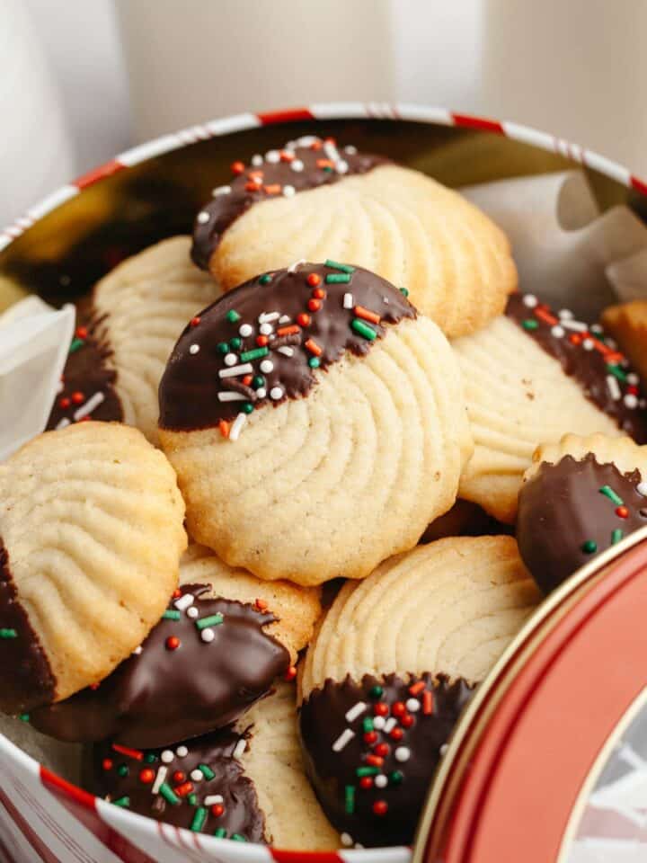 Chocolate dipped butter cookies with sprinkles in a tin.