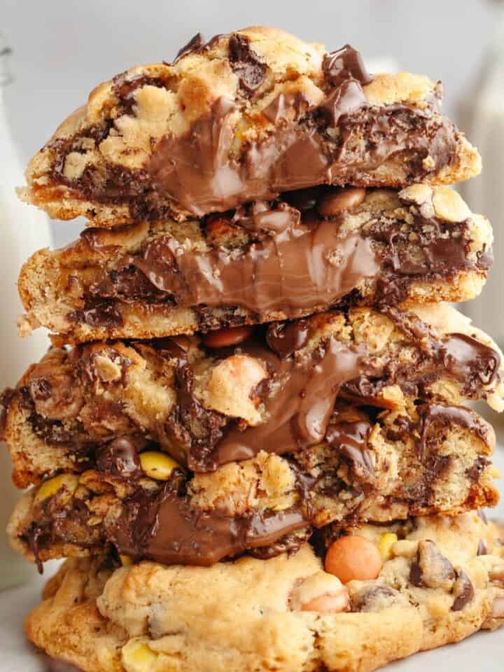 A stack of five peanut butter Nutella cookies, tour of the cookies are broken in half showing that they're stuffed with Nutella.