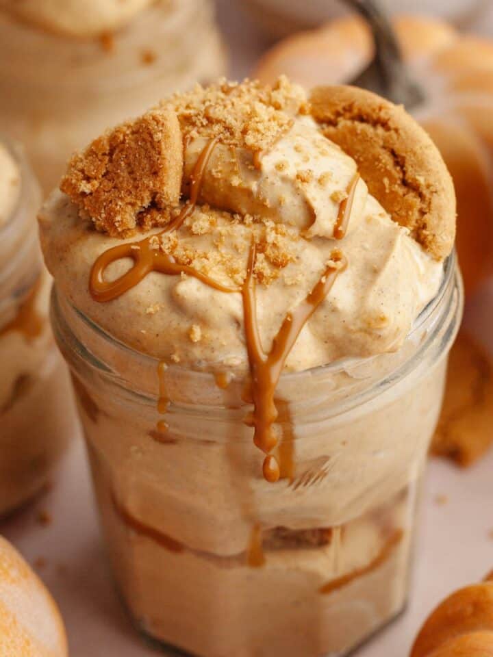 Pumpkin pie cups in mason jars, topped with crushed gingersnap cookies and drizzled cookie butter.