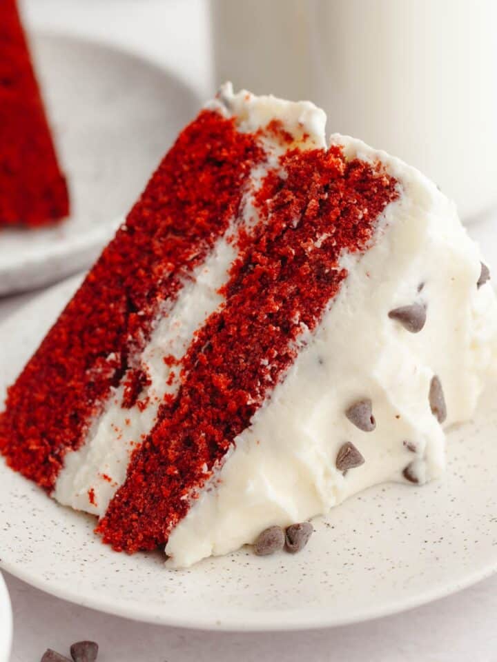 A slice of red velvet cake with chocolate chips and cream cheese frosting.
