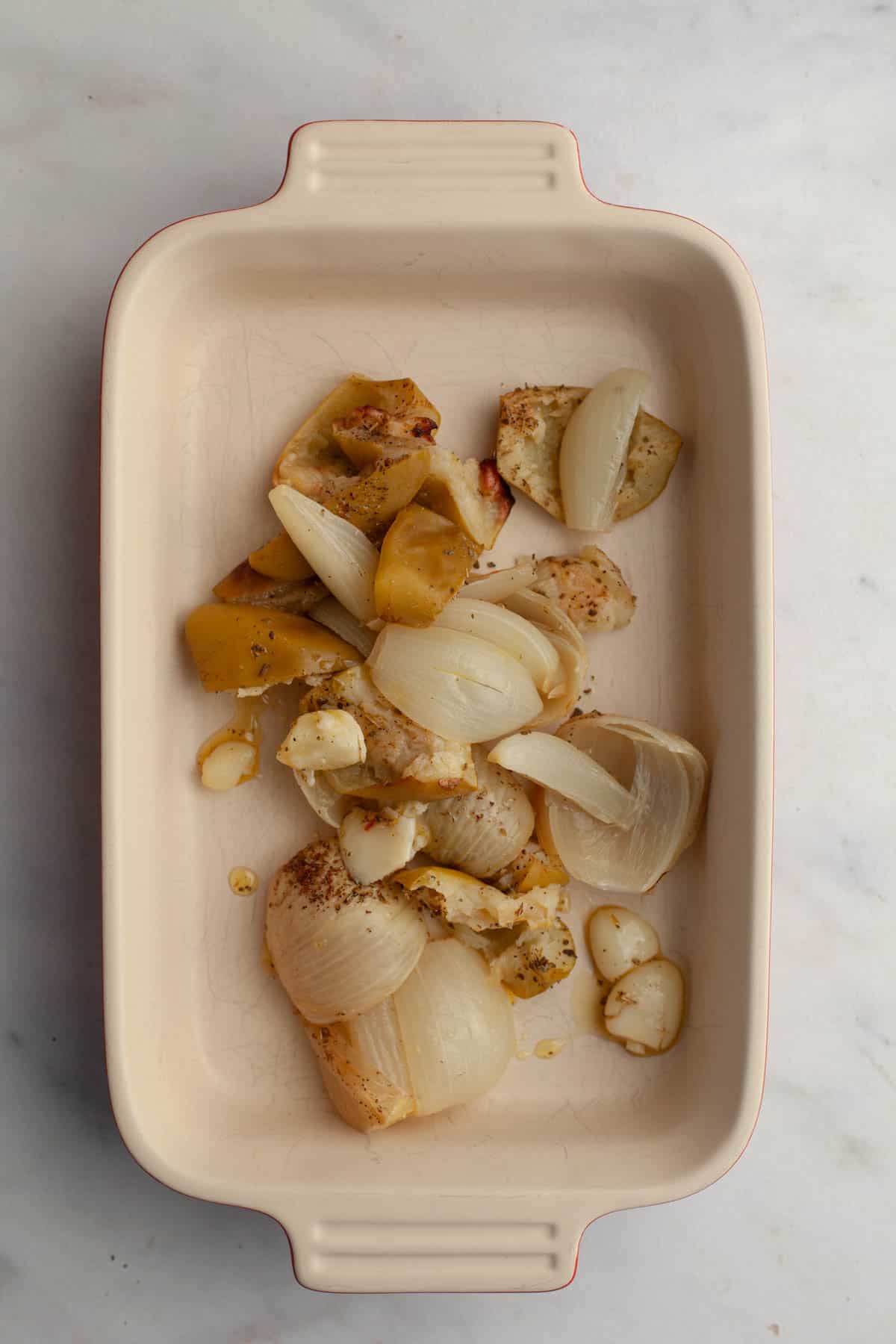 A small baking dish with roasted onions, garlic and apples in it.