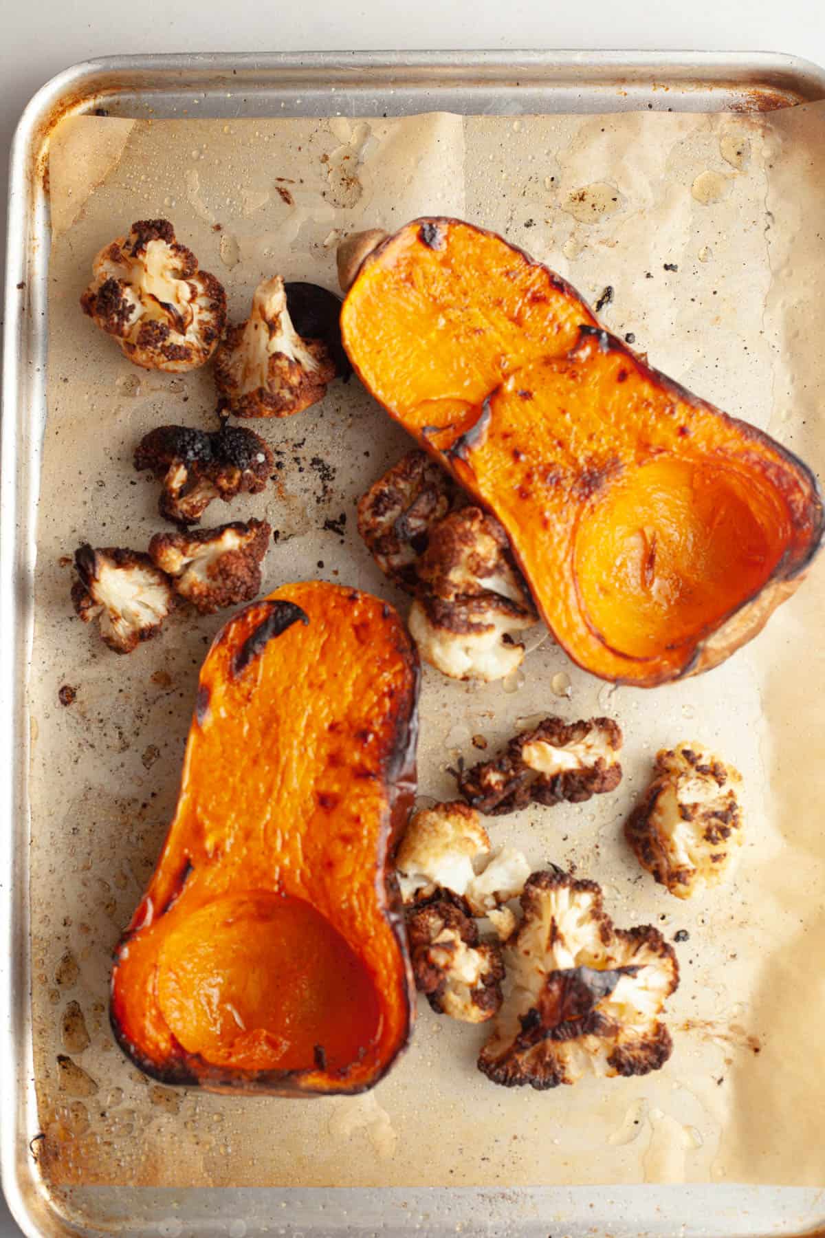 A sheet pan with roasted butternut squash cut in half, chopped onions and cauliflower florets with olive oil and pepper.