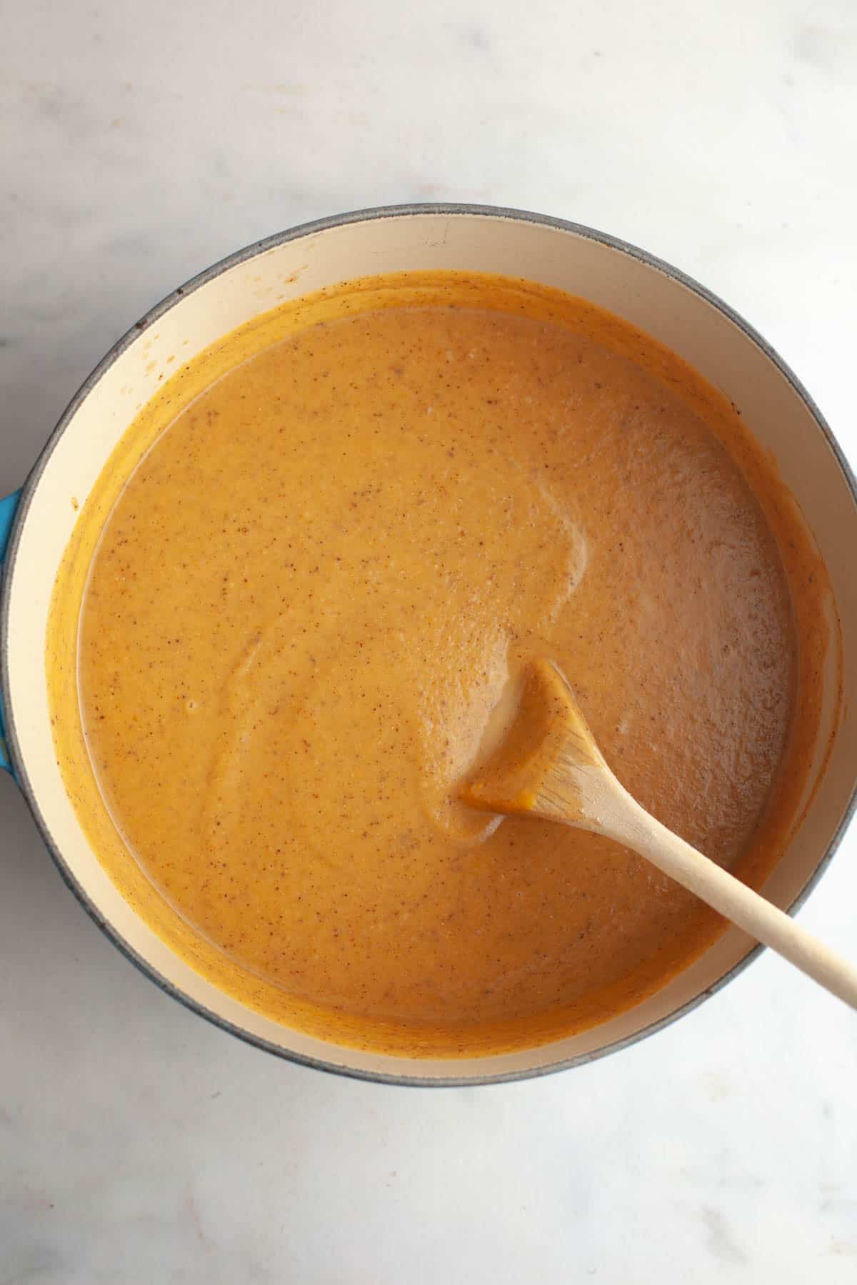 A large dutch oven with cauliflower butternut squash soup in it and a wooden spoon.