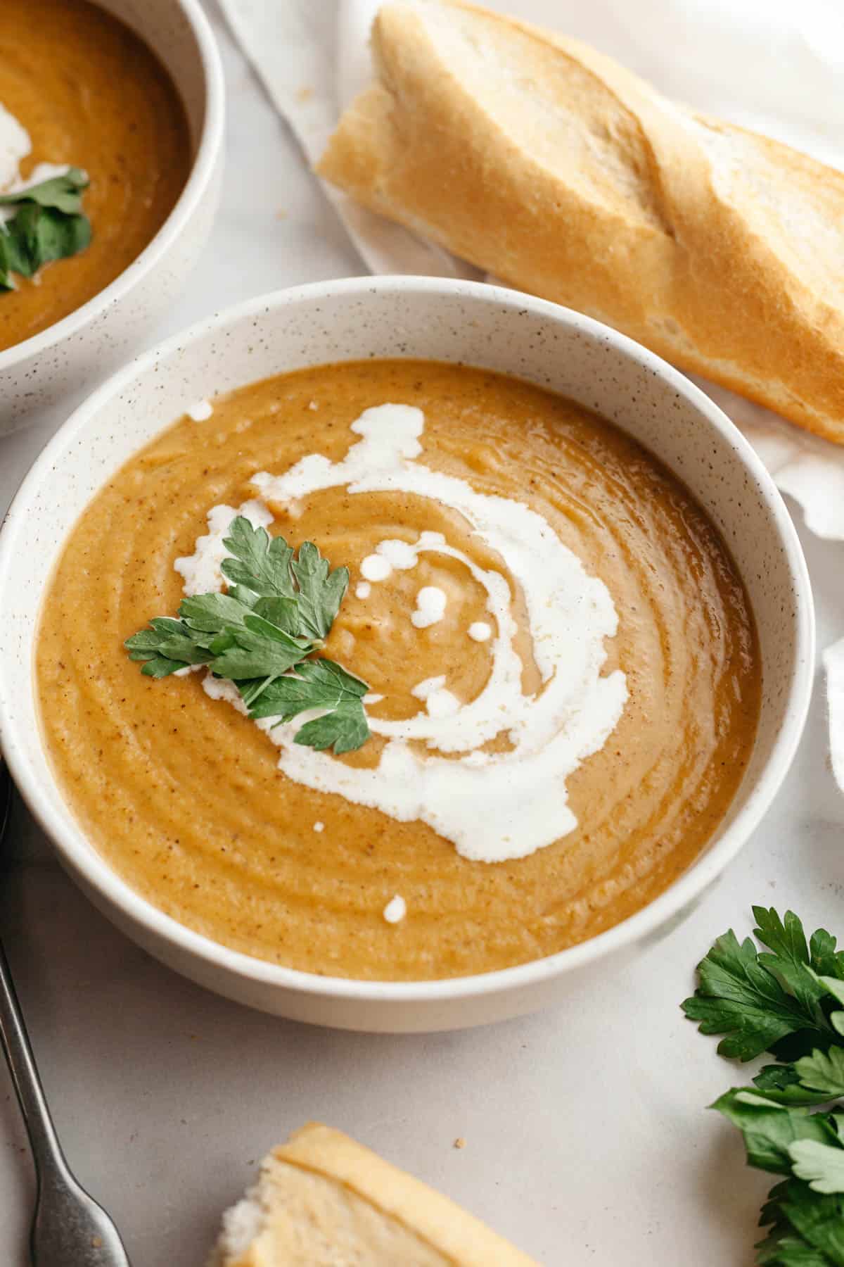 A white soup bowl with butternut squash cauliflower soup, drizzled with cream and garnished with herbs.