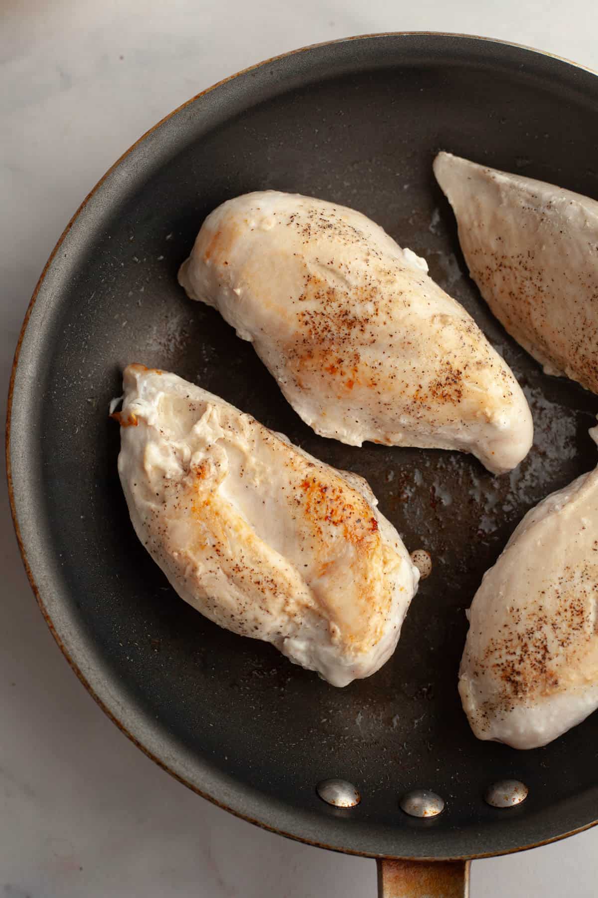 A skillet with cooked chicken breasts.