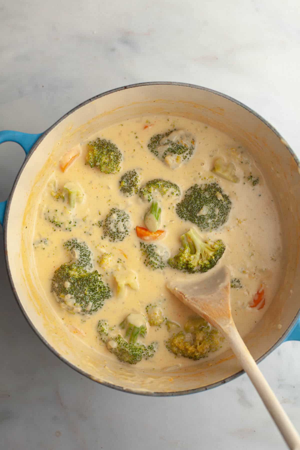 A large dutch oven with broccoli and cheddar soup in it, and a wooden spoon.