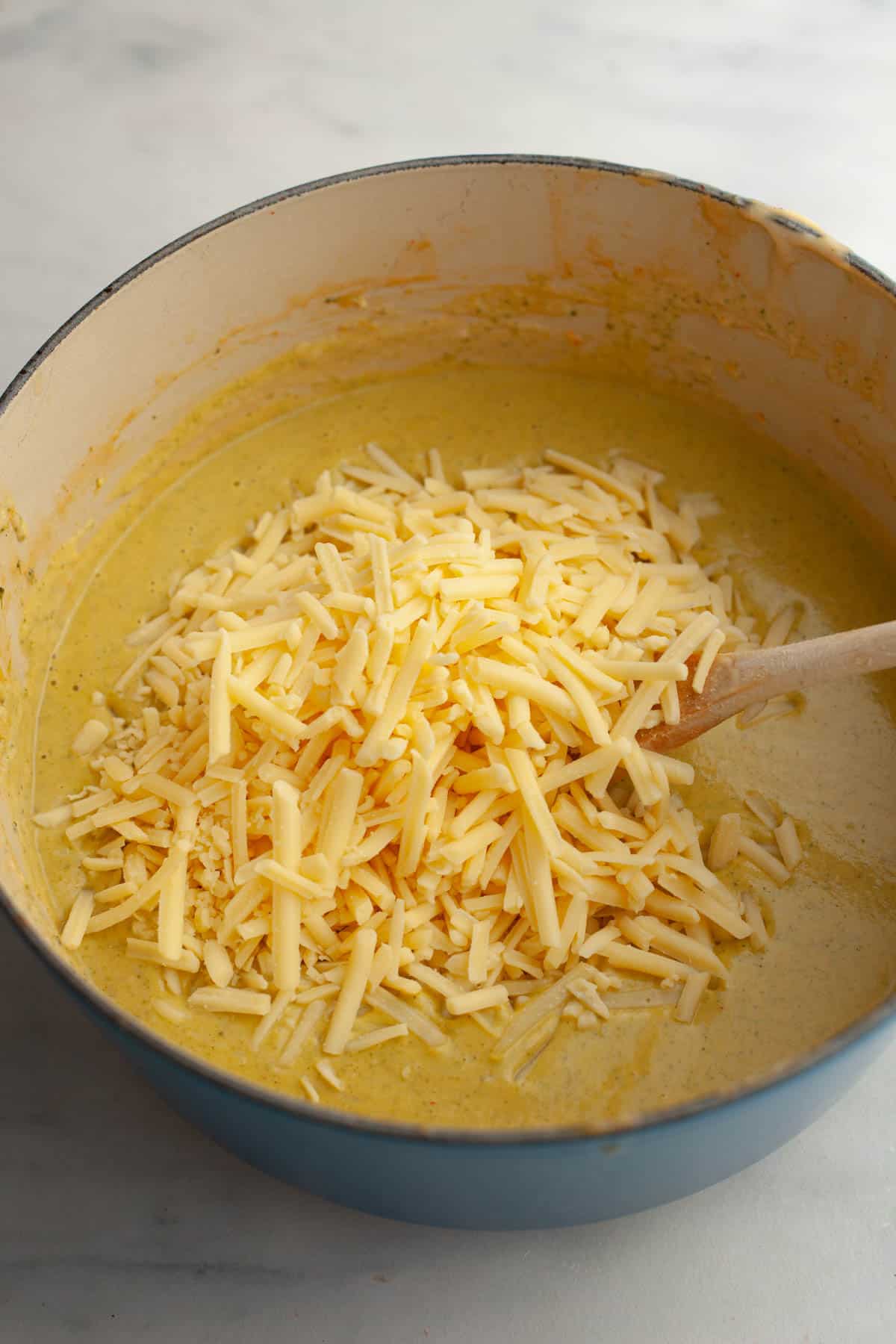 A large pot with broccoli soup and grated cheddar cheese.