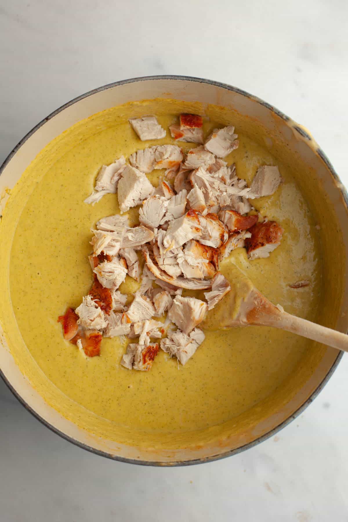A large dutch oven with broccoli cheddar soup and pieces of chicken.