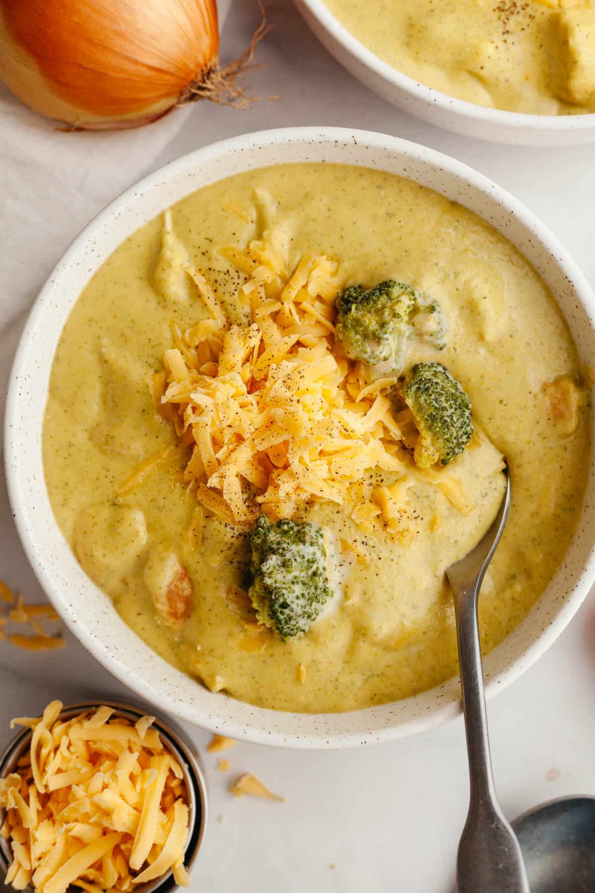 A bowl of chicken and broccoli cheddar soup, topped with shredded cheddar cheese.