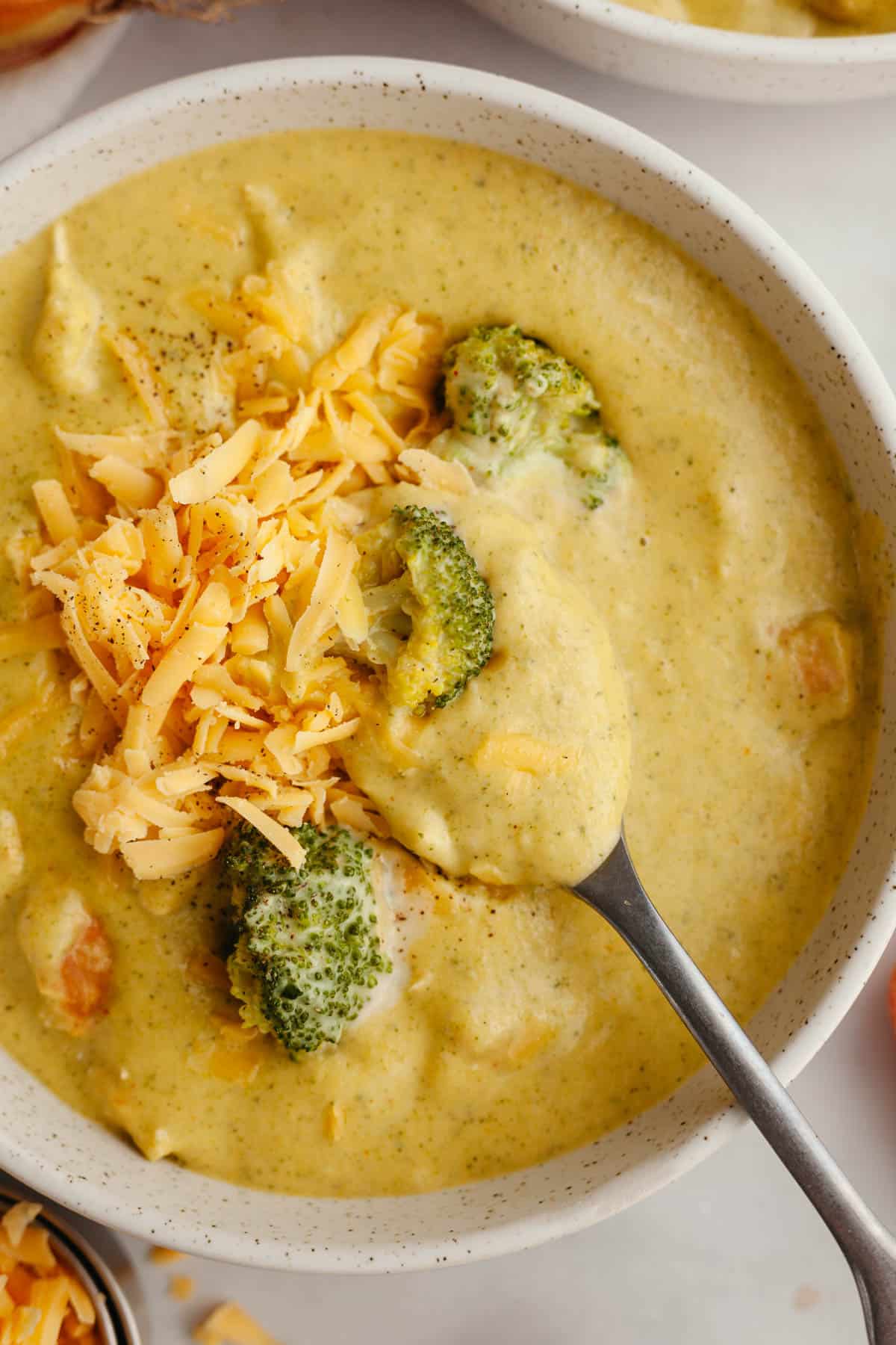 A bowl of chicken and broccoli cheddar soup, topped with shredded cheddar cheese.