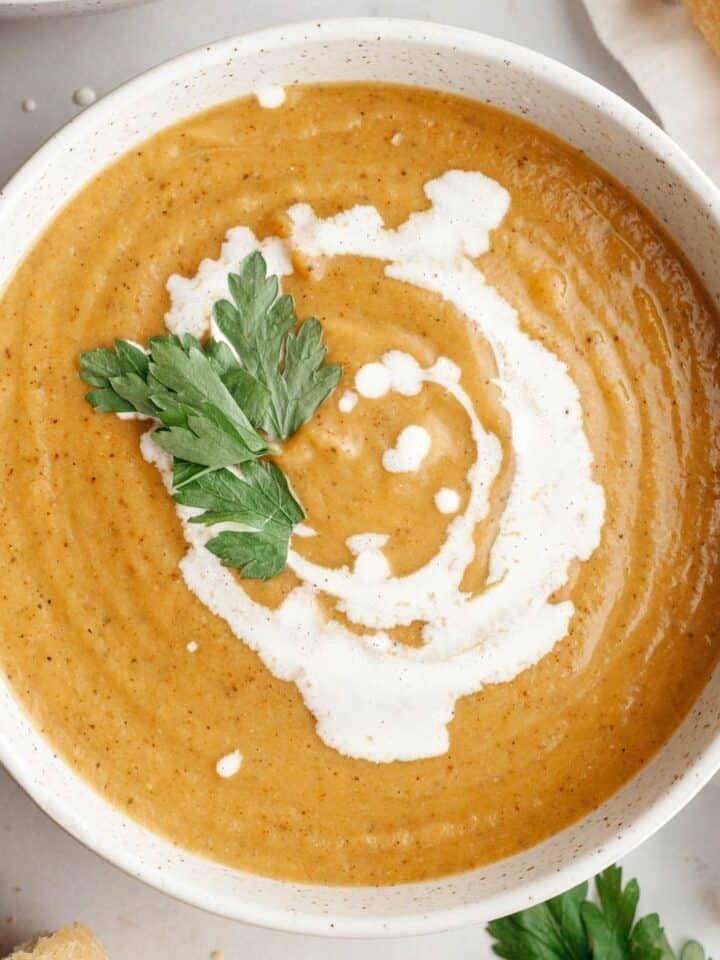 A white soup bowl with butternut squash cauliflower soup, drizzled with cream and garnished with herbs.
