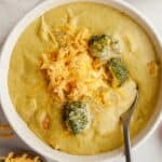 A bowl of chicken and broccoli cheddar soup, topped with shredded cheddar cheese.