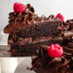 A slice of chocolate cake with chocolate ganache being lifted out with a silver cake server.