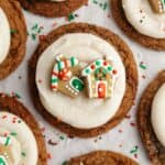 A close up of a gingerbread cookie frosted with cream cheese frosting and a small gingerbread house decoration.