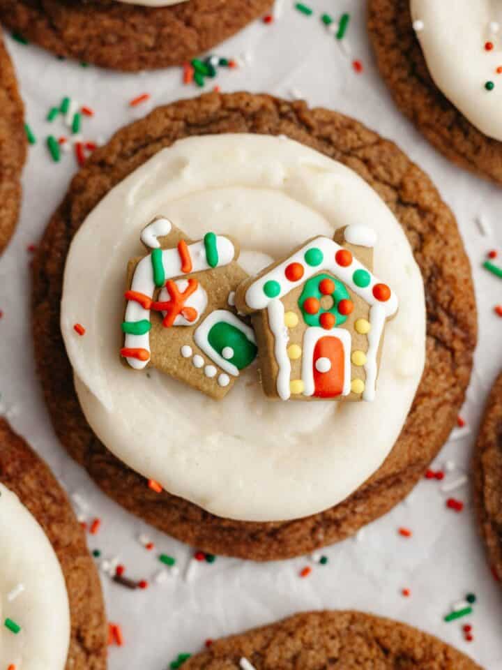 A close up of a gingerbread cookie frosted with cream cheese frosting and a small gingerbread house decoration.