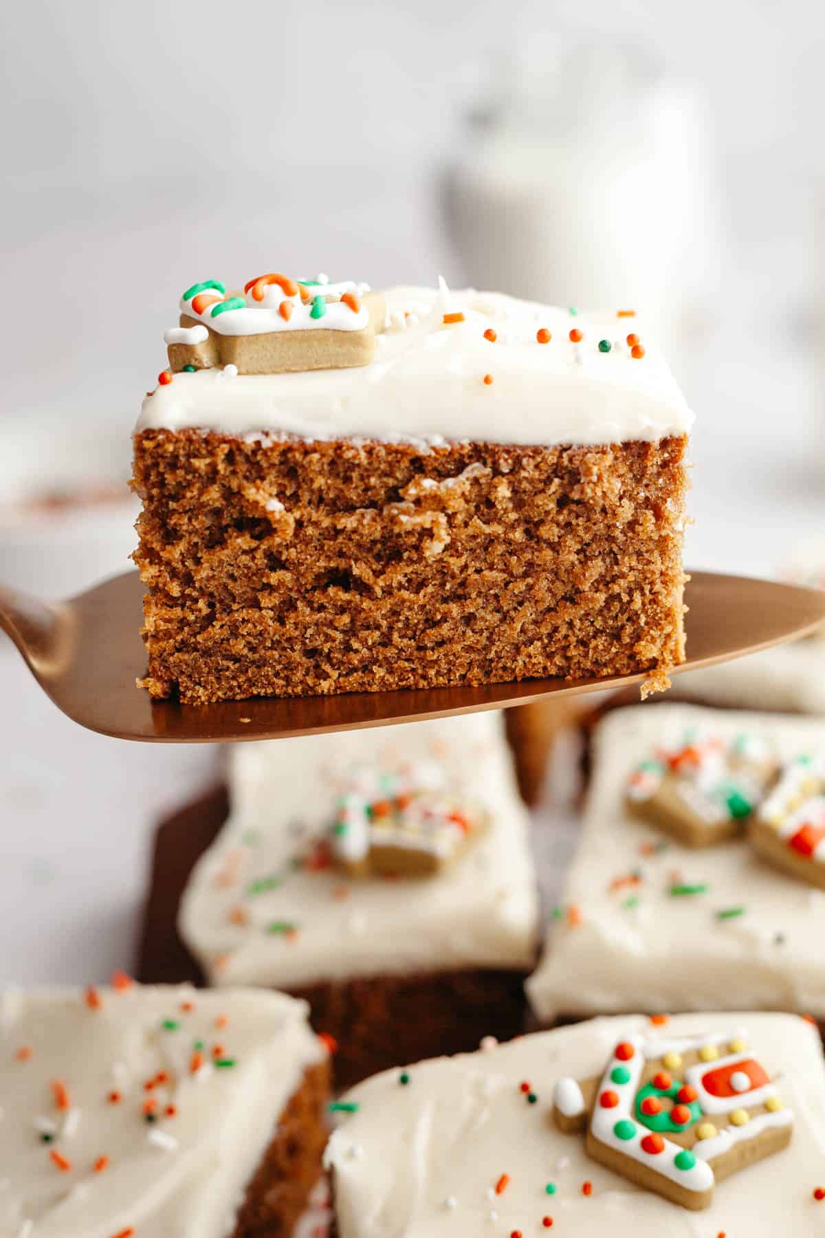 A cake server lifting up a slice of gingerbread cake with cream cheese frosting.