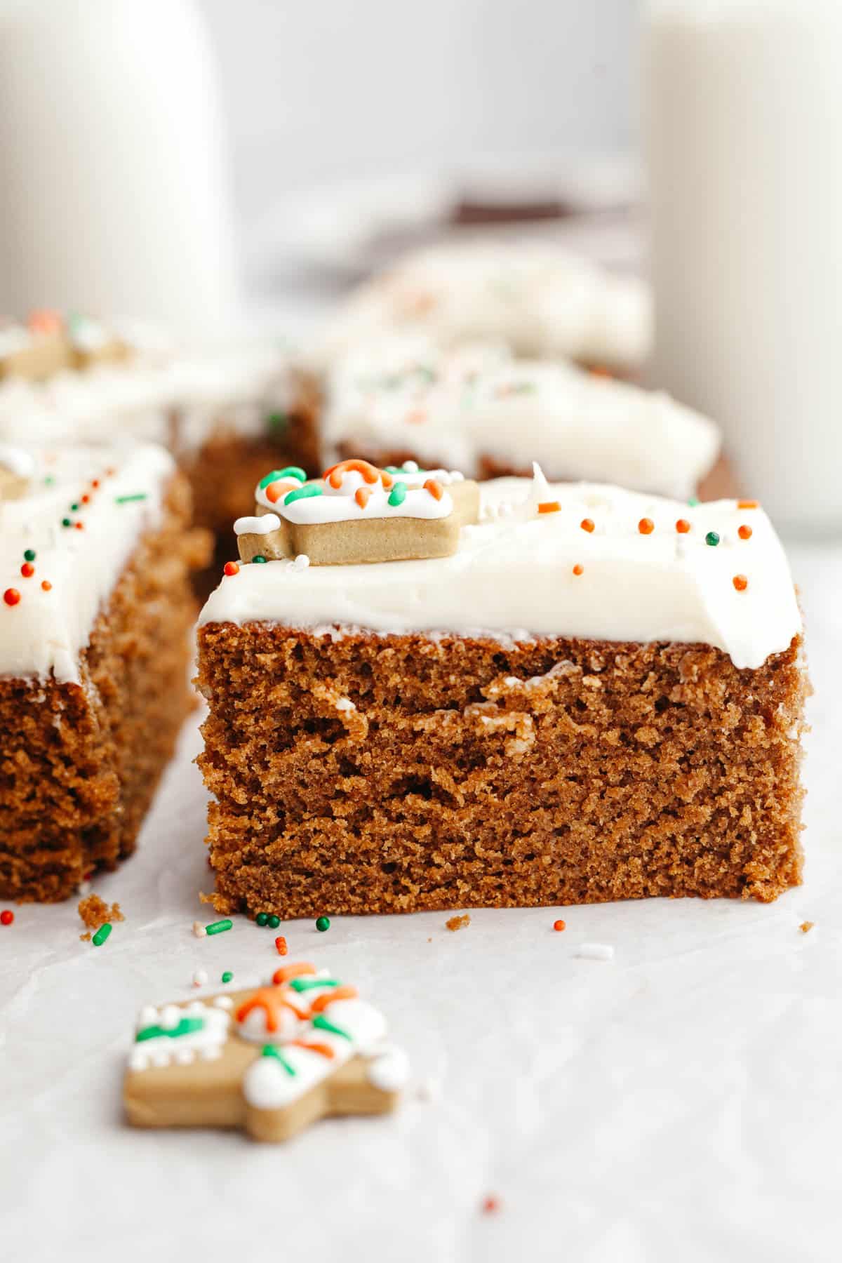 A slice of gingerbread cake with cream cheese frosting on parchment paper.