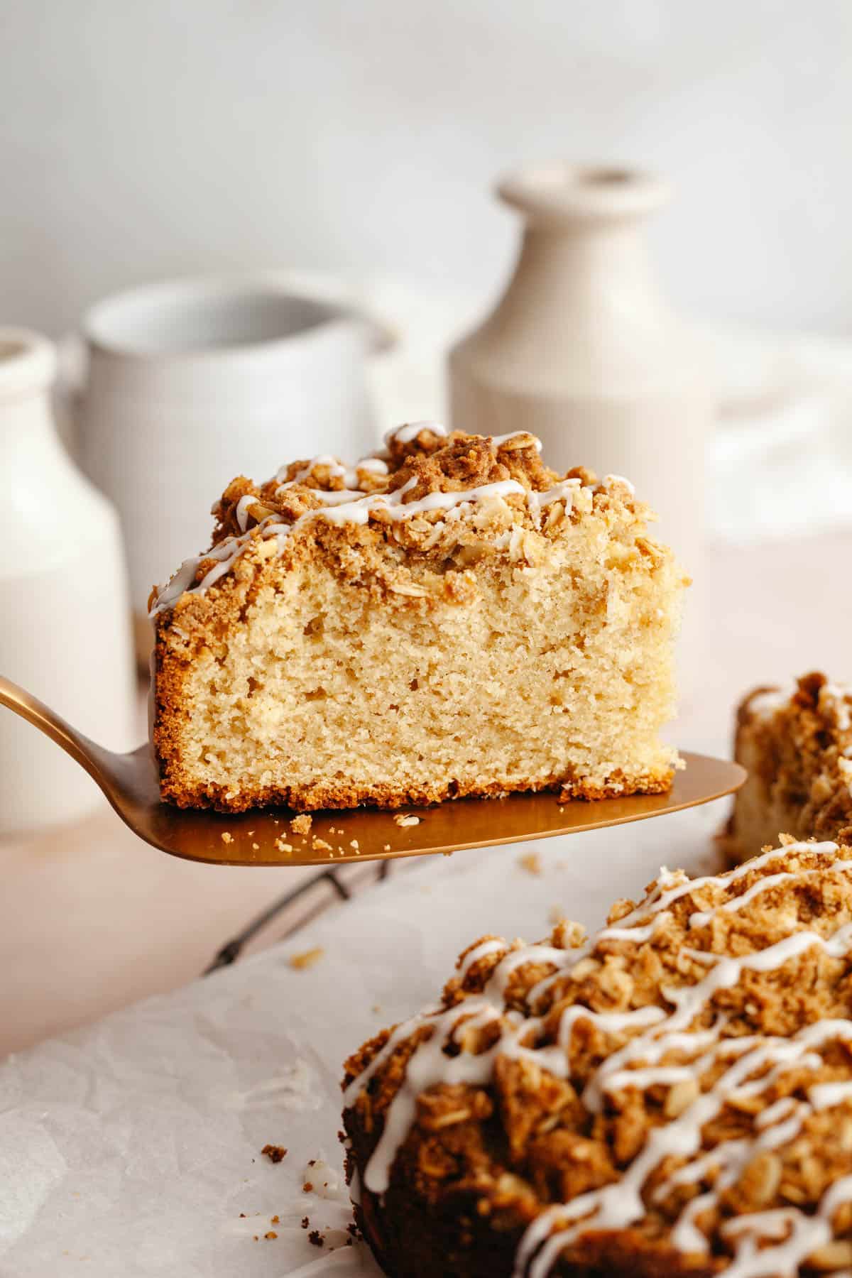 A slice of cardamom almond cake being lifted out with a cake server, drizzled with a glaze.