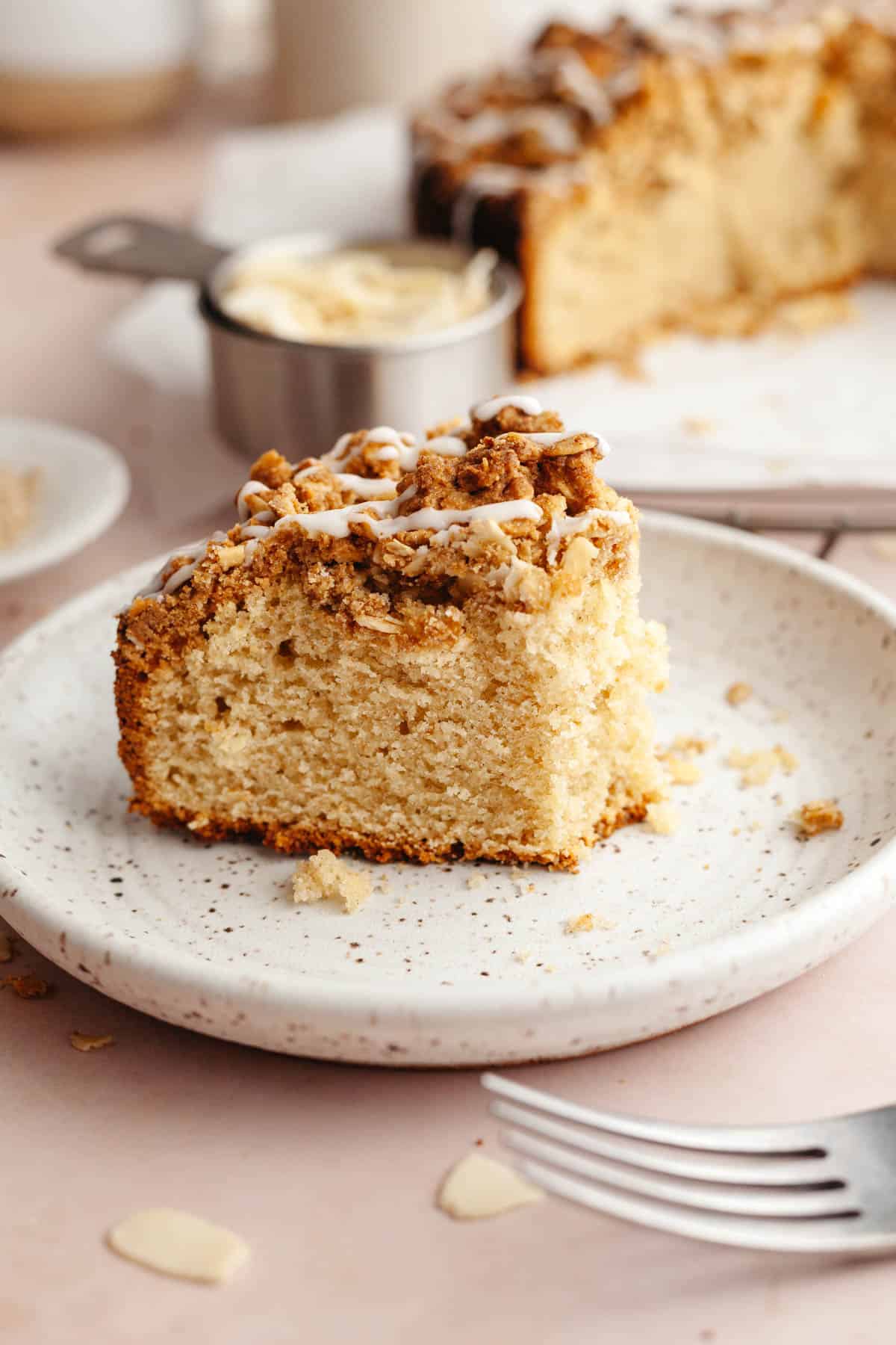 A slice of almond cardamom cake on a plate, a bite has been taken out of it.