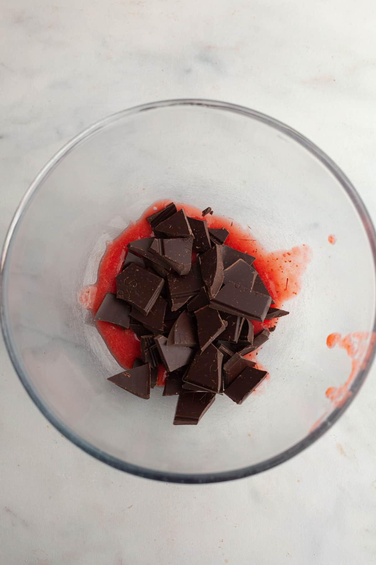 Chopped chocolate and strawberry puree in a glass bowl.