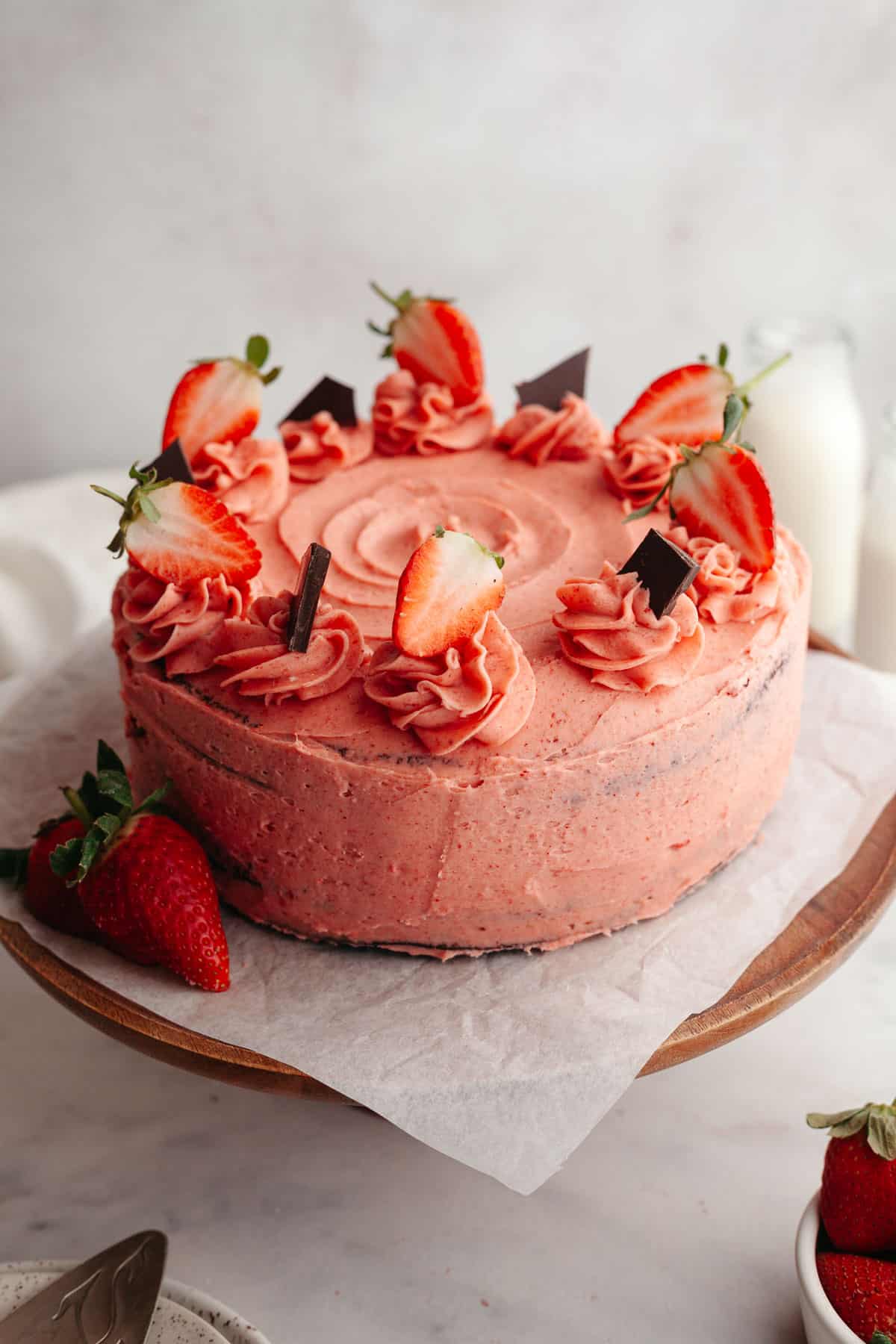 A chocolate covered covered in strawberry frosting on a cake stand.