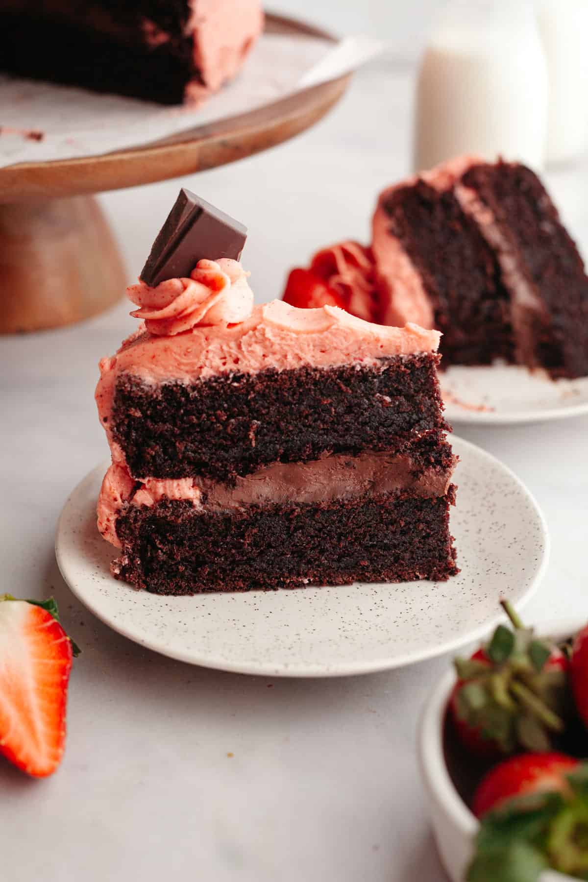 A chocolate cake covered in strawberry frosting with chocolate filling on a small plate.