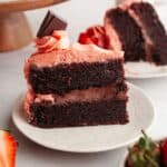 A slice of chocolate cake with strawberry ganache filling and strawberry frosting on a small plate.