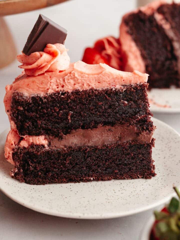 A slice of chocolate cake with strawberry ganache filling and strawberry frosting on a small plate.