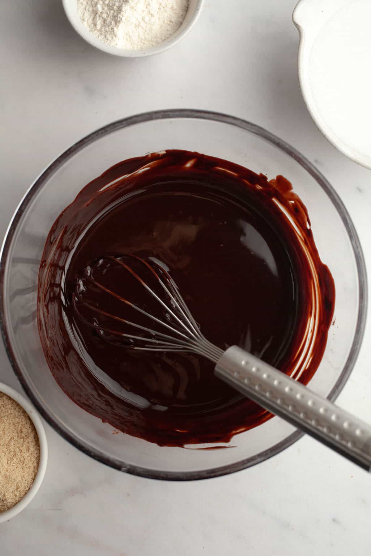 Melted chocolate and butter in a glass bowl with a whisk.