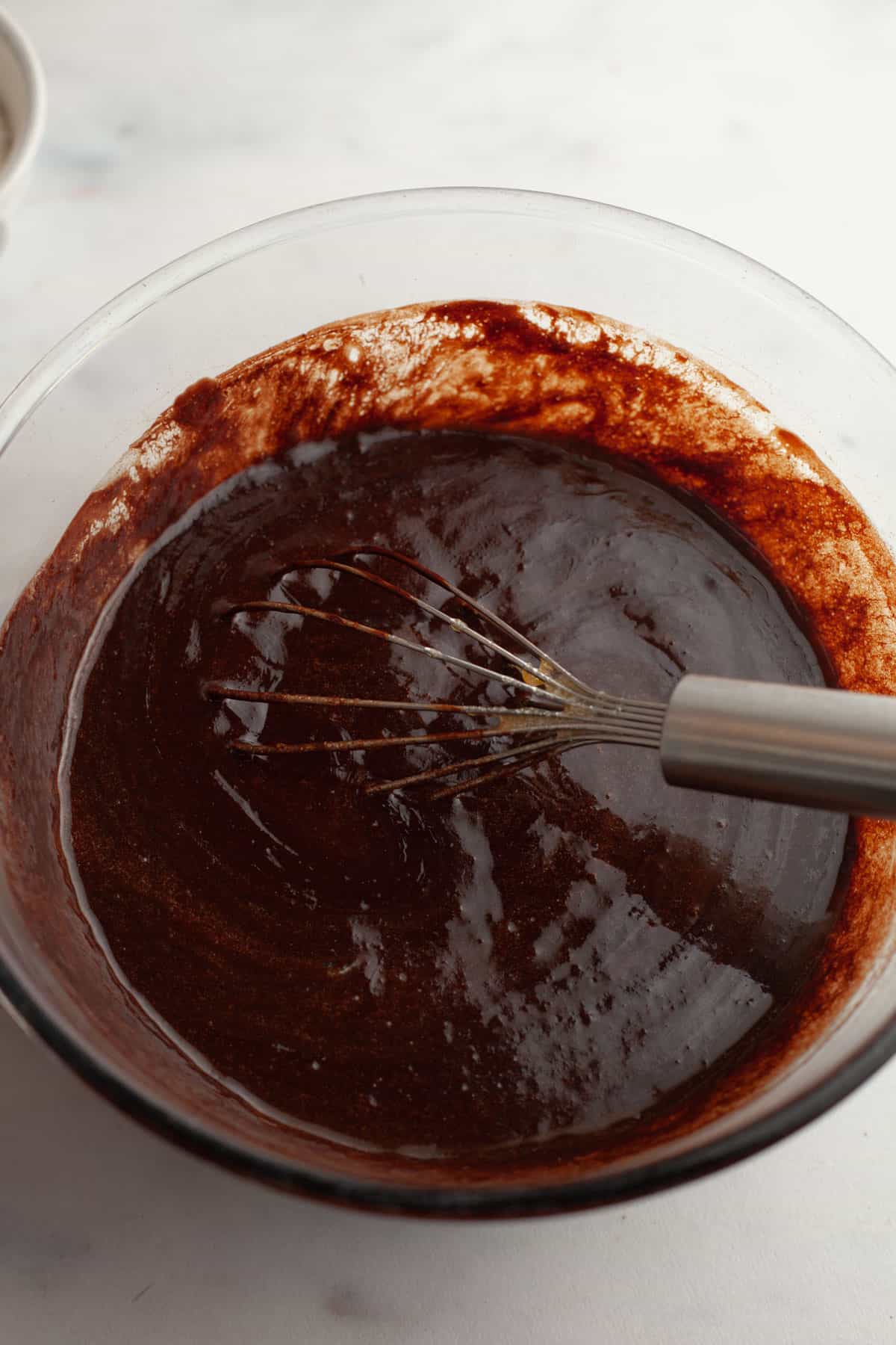 A glass bowl with brownie batter in it and a whisk.