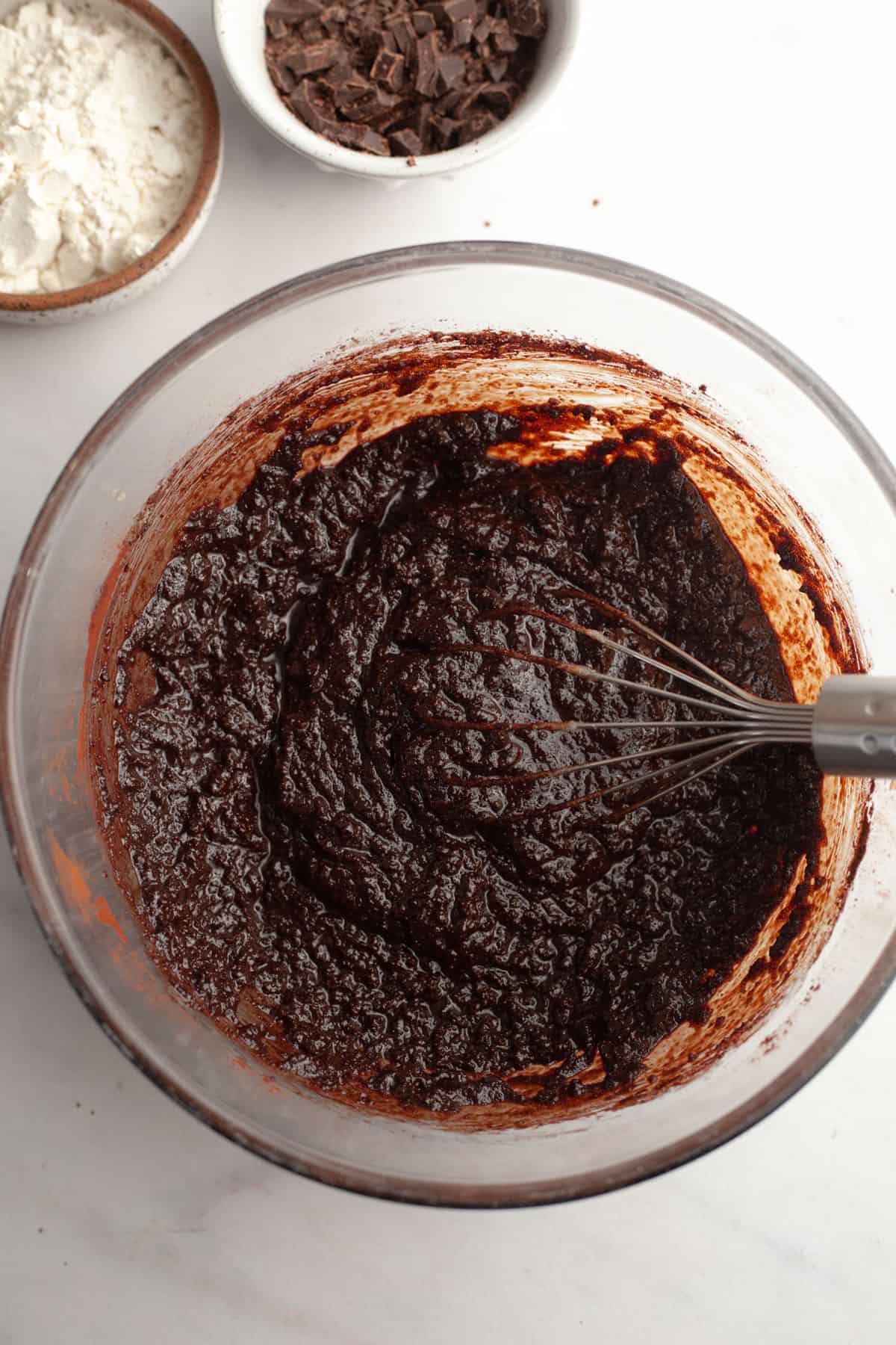 A glass bowl with brownie batter in it and a whisk.