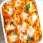 Baked vodka pasta in a white dish topped with basil leaves.