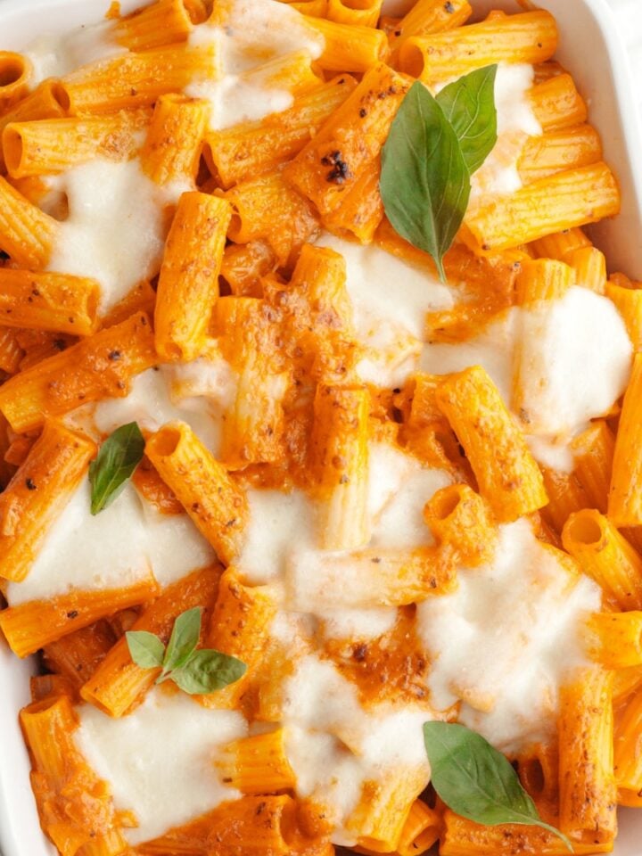 Baked vodka pasta in a white dish topped with basil leaves.