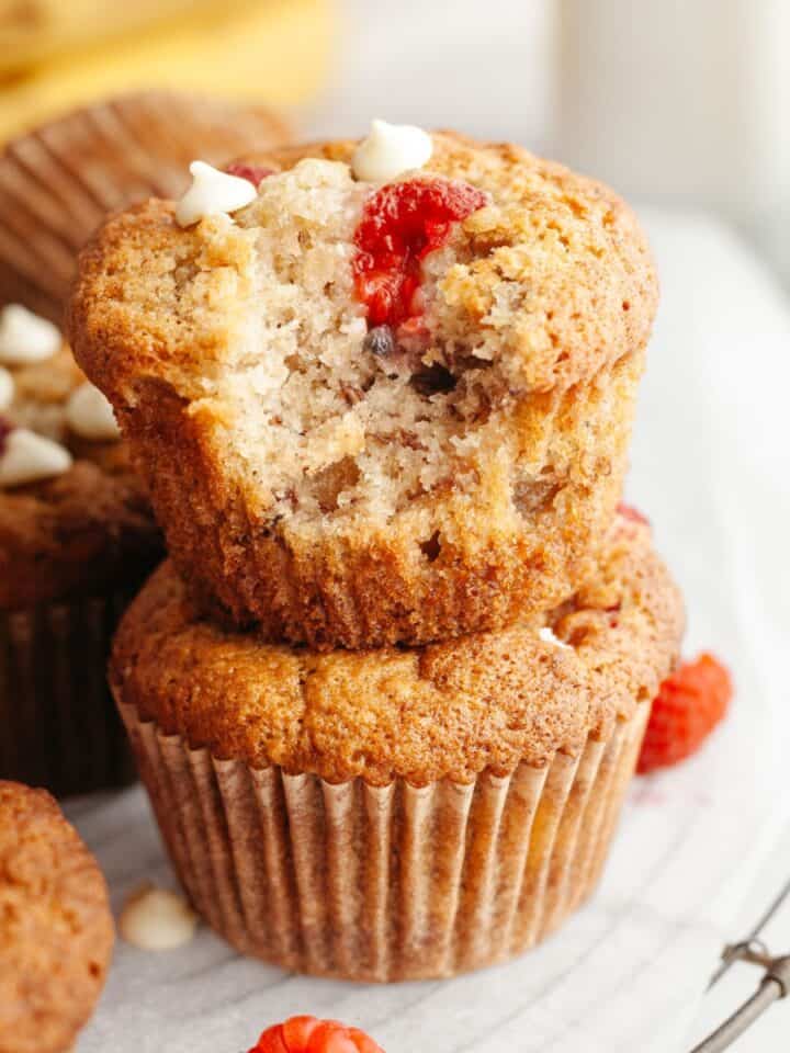 Two raspberry banana muffins stacked on top of each other, one has a bite taken out of it.