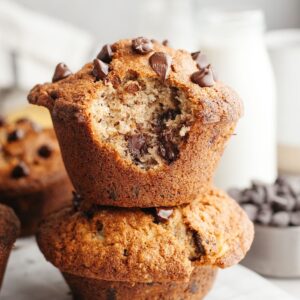 Two jumbo banana muffins with chocolate chips stacked on top of each other, one has a bite taken out of it.