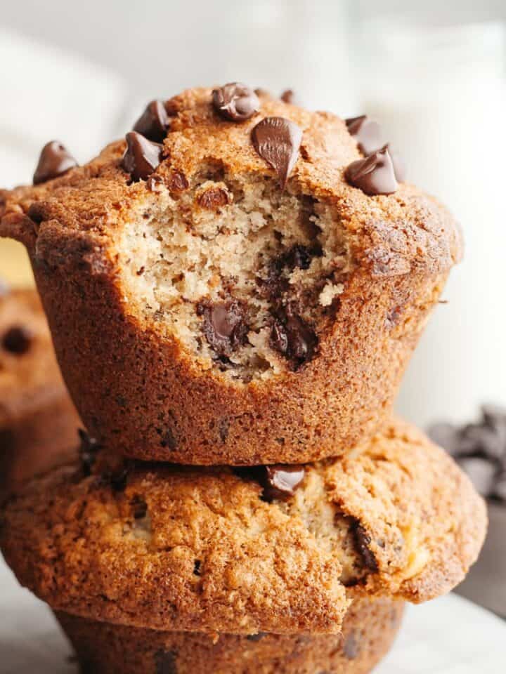 Two jumbo banana muffins with chocolate chips stacked on top of each other, one has a bite taken out of it.