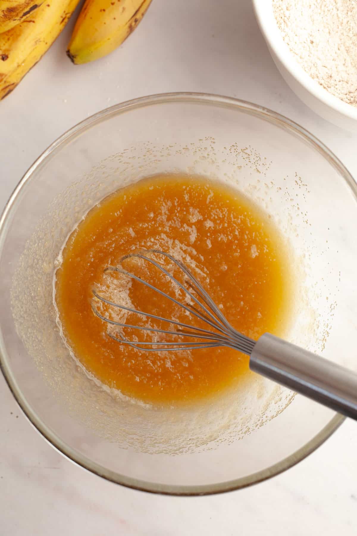 A bowl with a whisk, inside is melted butter and sugar.